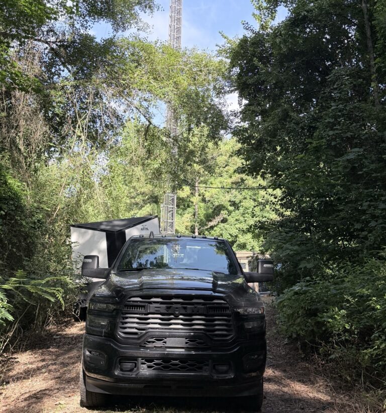 Tower Tigers Crew truck and equipment trailer heading down a wooded access trail to a cell tower site